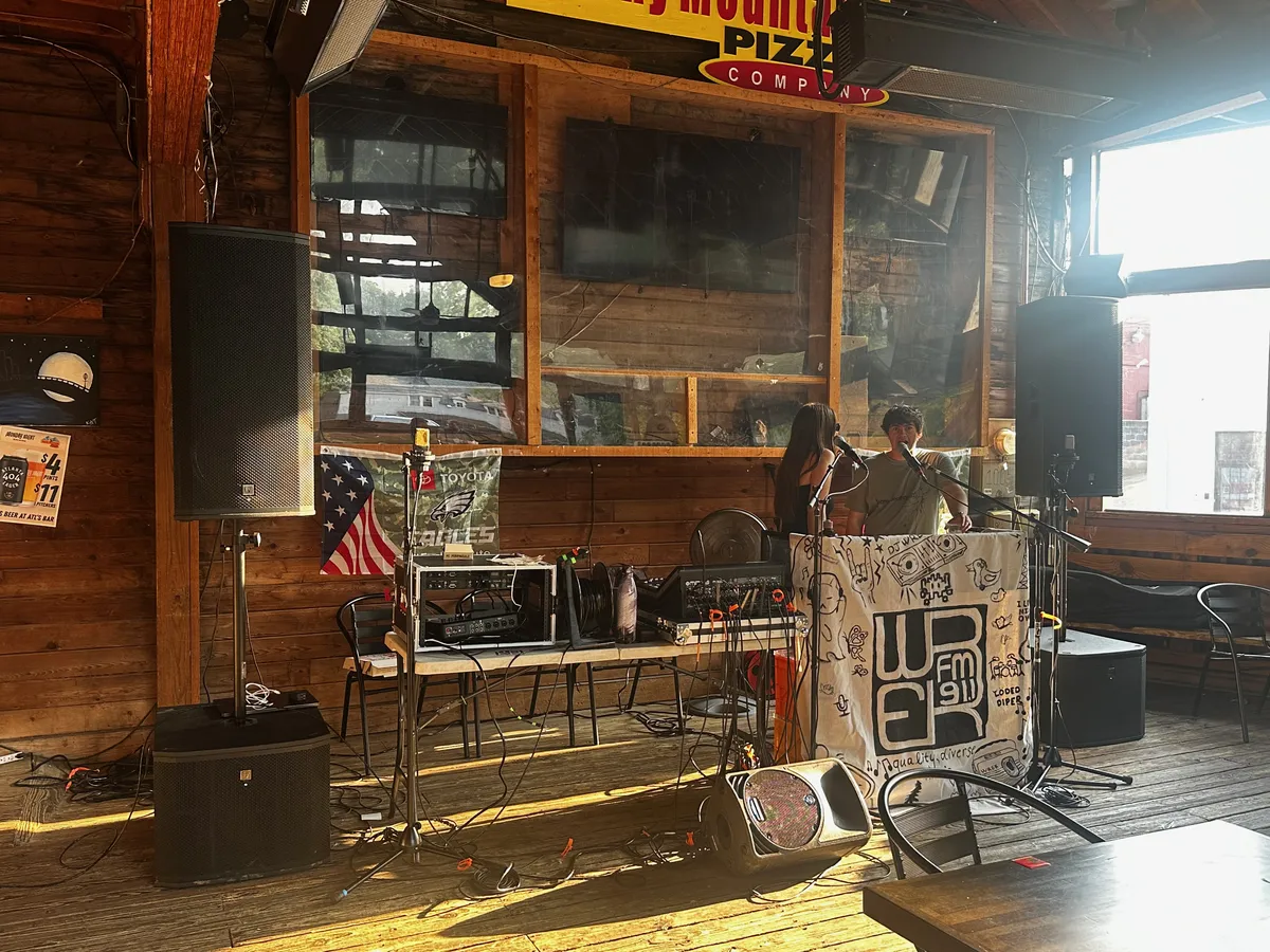 An indoor WREK broadcast table with microphones, a WREK banner, and PA speakers.