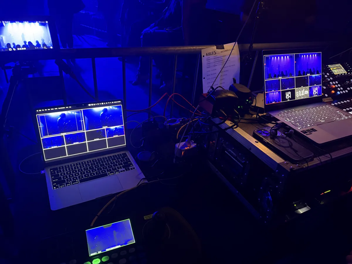 Video-production laptops, monitors, and a switcher running at a blue-lit live event.