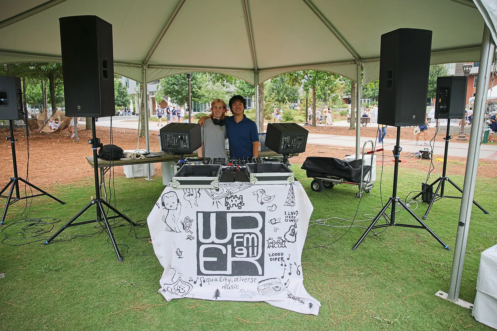 Two student DJs running decks beside a WREK banner and PA speakers under an outdoor tent.